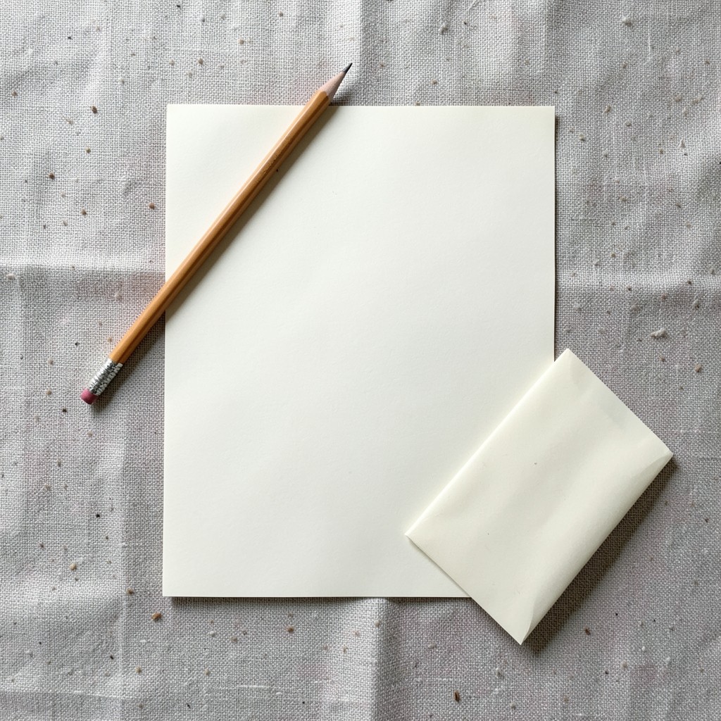 Blank paper, a pencil, and a small sealed envelope on linen